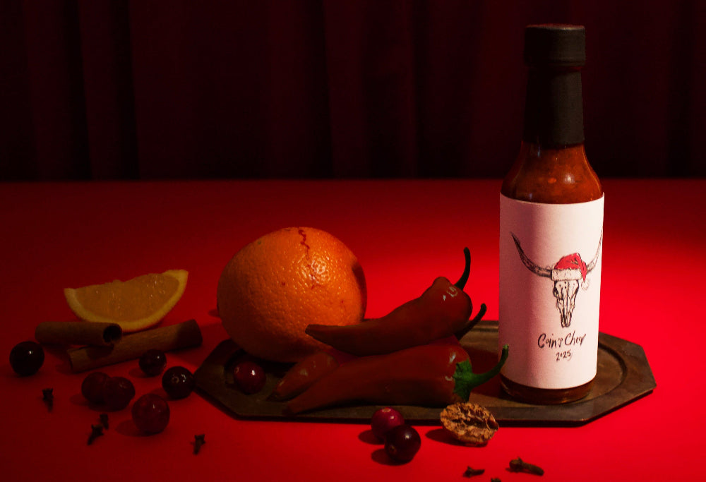 Hot sauce bottle on a wooden board with fruits and spices against a red curtain background