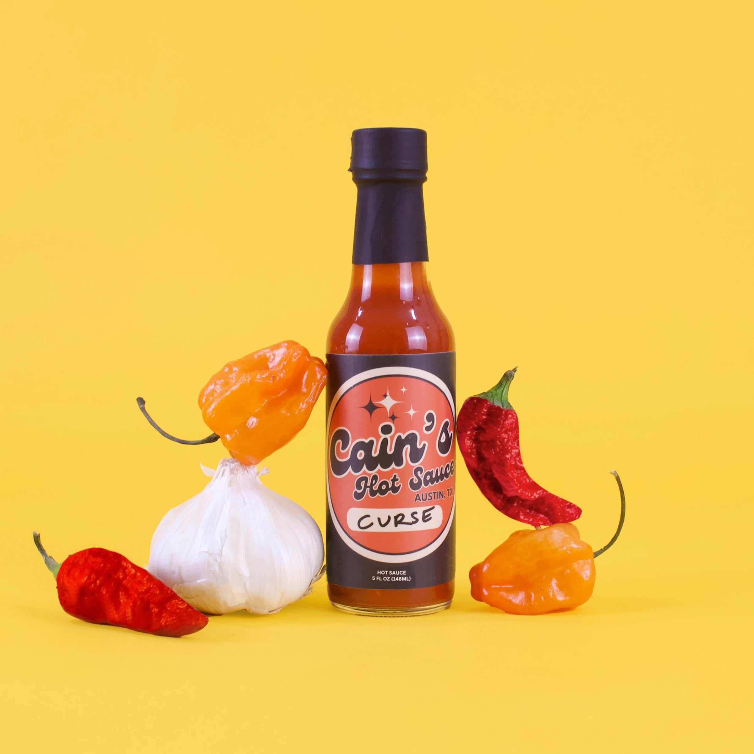 Bottle of 'Cain's Hot Sauce Curse' with chili peppers on a yellow background