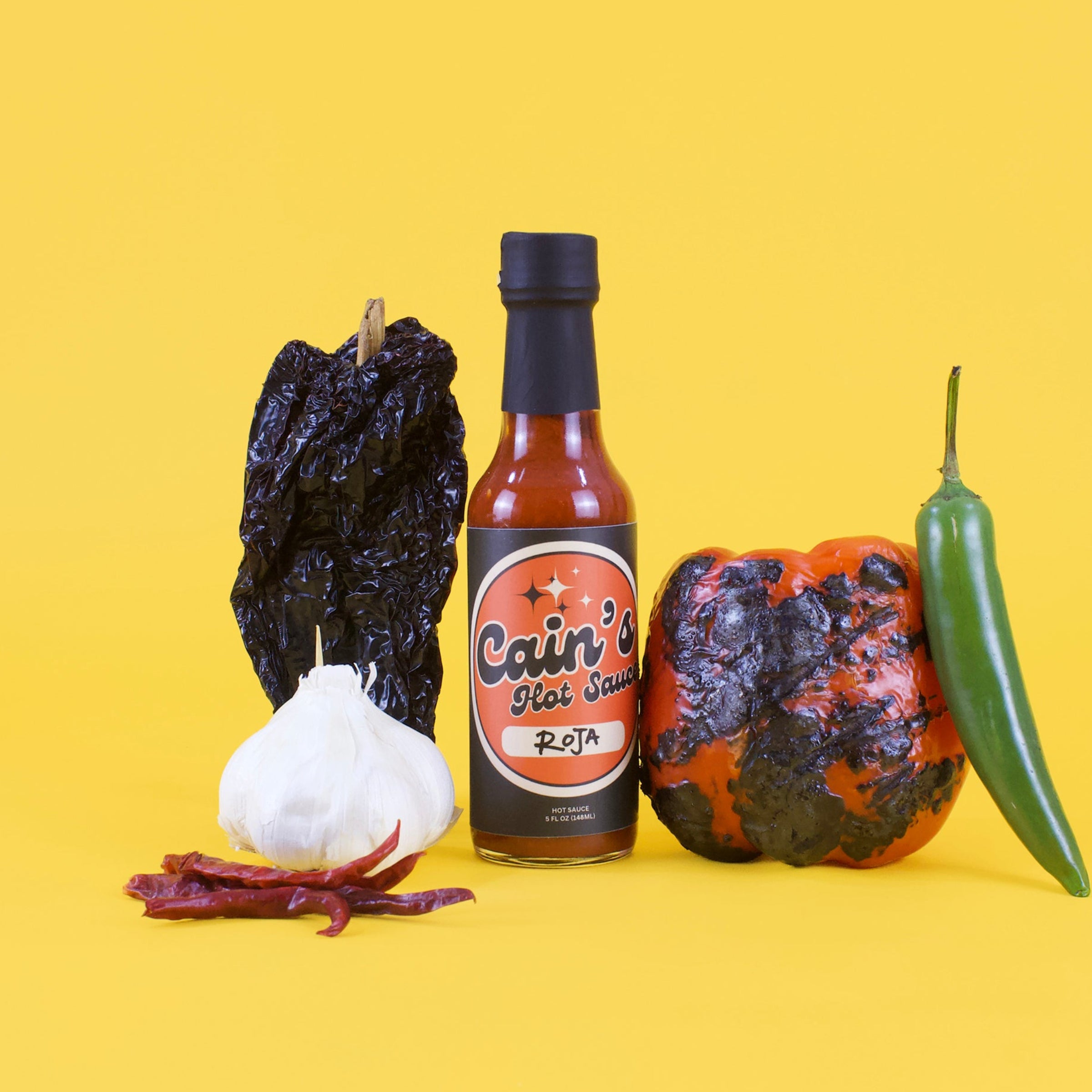 Hot sauce bottle with dried chilies and a green jalapeño pepper on a yellow background